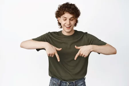 happy_young_man_with_curly_hair_pointing_looking_down_smiling_laughing
